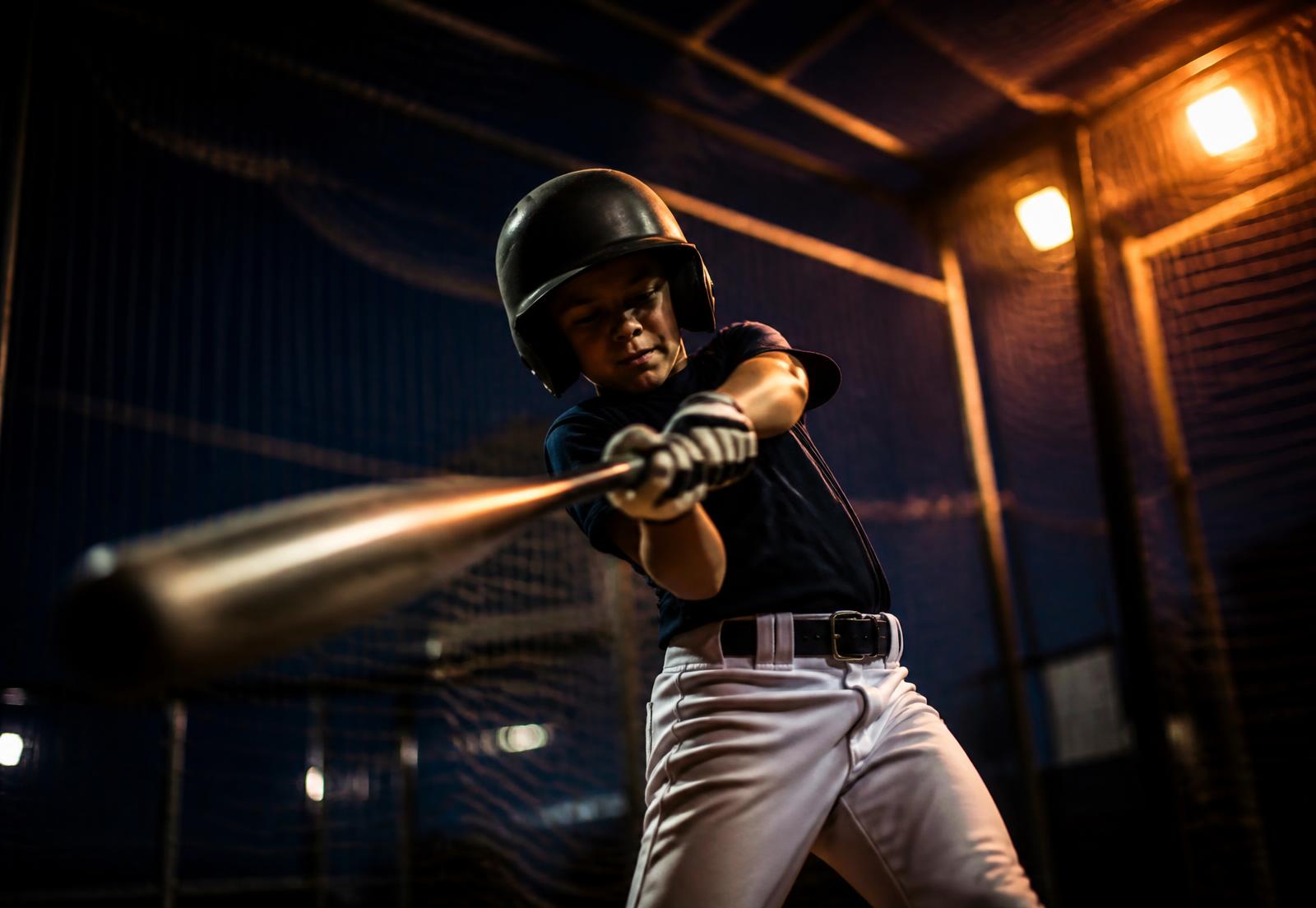 Young baseball player swinging in a lit indoor batting cage
